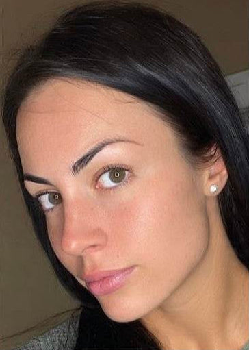 Close-up of a woman with dark hair and earrings against a neutral background using oreva skin care